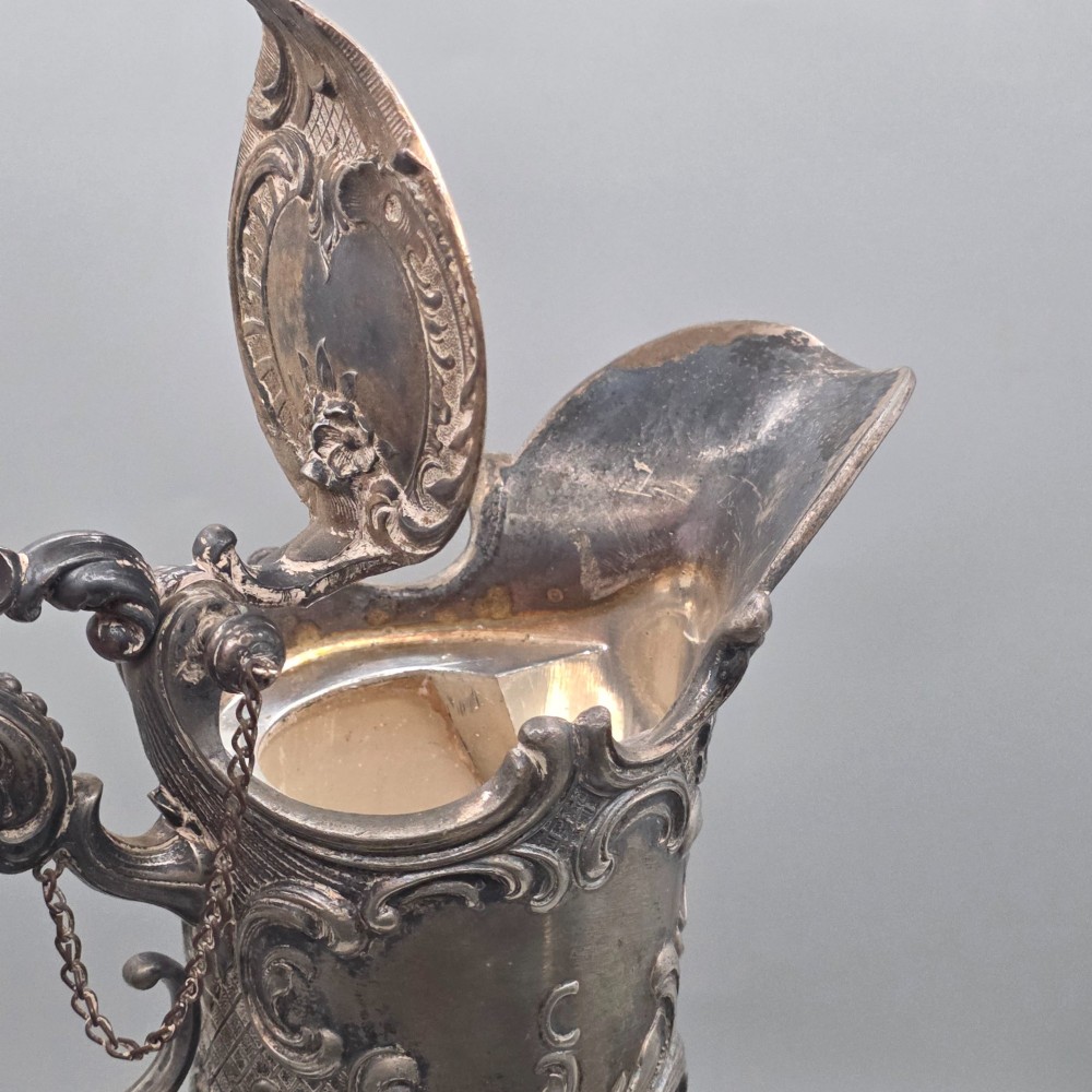 An antique French Rococo style silver-plated claret jug featuring a tapered ribbed clear glass body and an ornate scrolling silver spout and handle. View IX