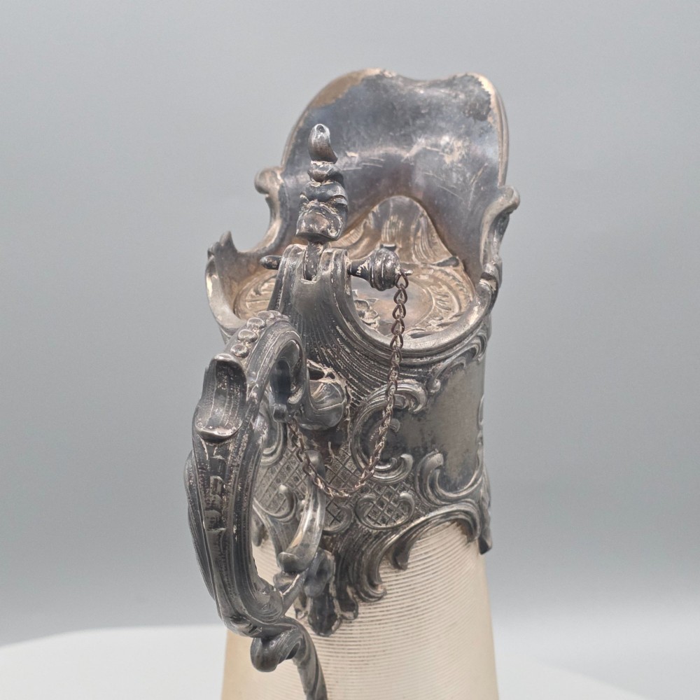 An antique French Rococo style silver-plated claret jug featuring a tapered ribbed clear glass body and an ornate scrolling silver spout and handle. View X