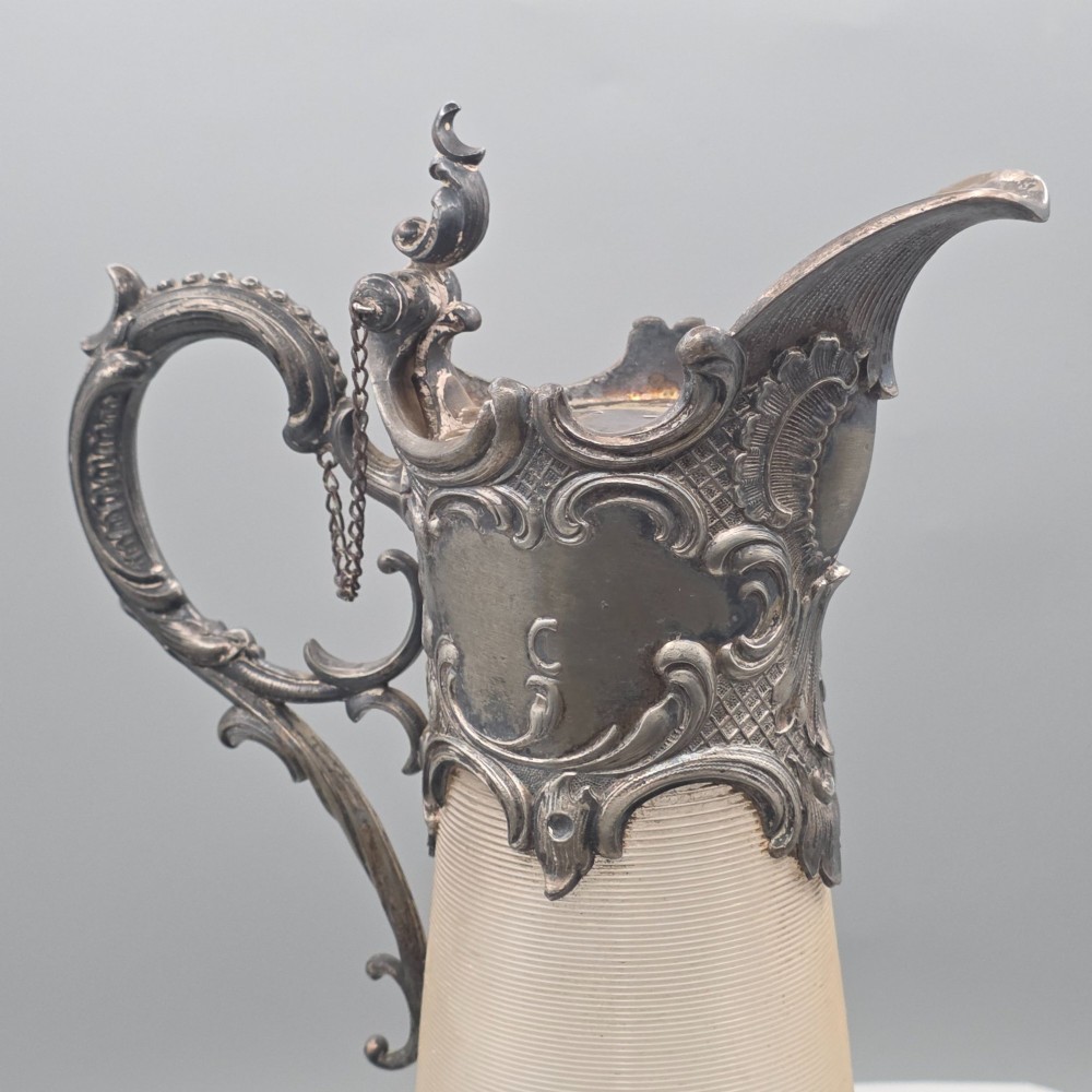 An antique French Rococo style silver-plated claret jug featuring a tapered ribbed clear glass body and an ornate scrolling silver spout and handle. View XI