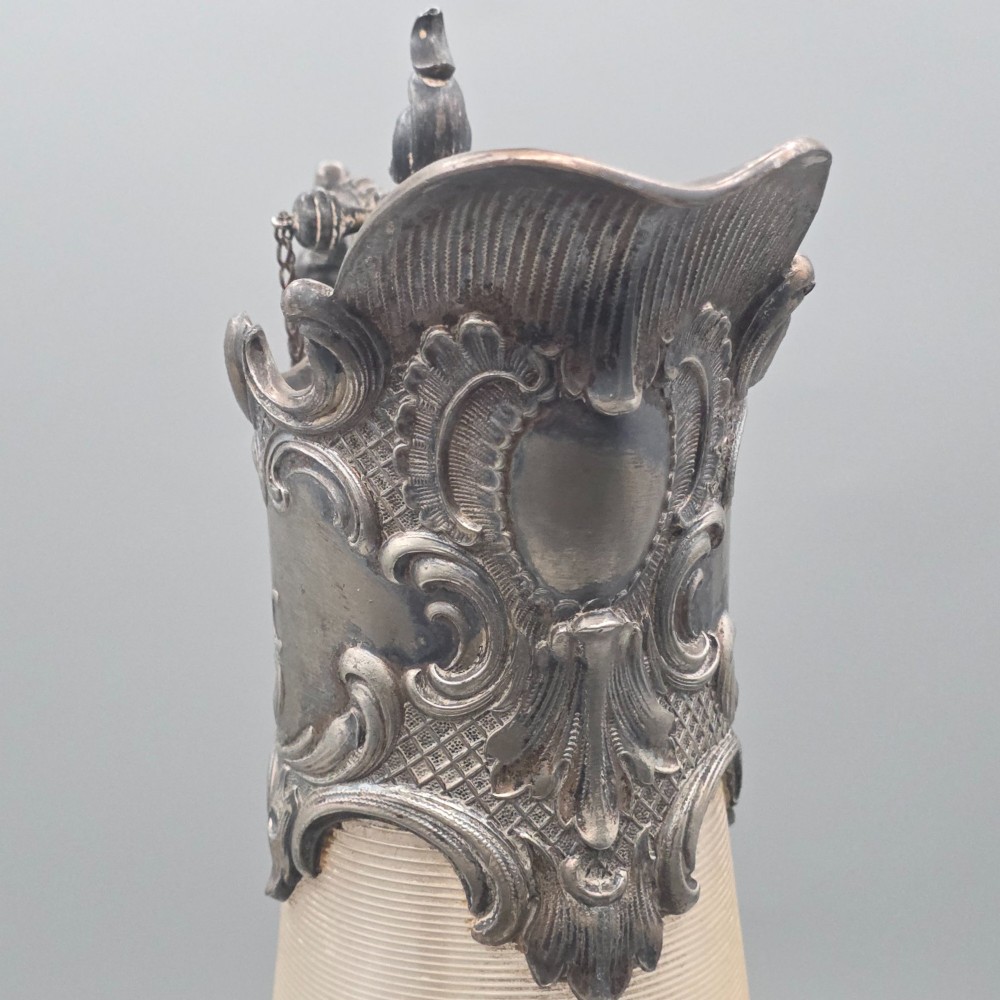 An antique French Rococo style silver-plated claret jug featuring a tapered ribbed clear glass body and an ornate scrolling silver spout and handle. View XII
