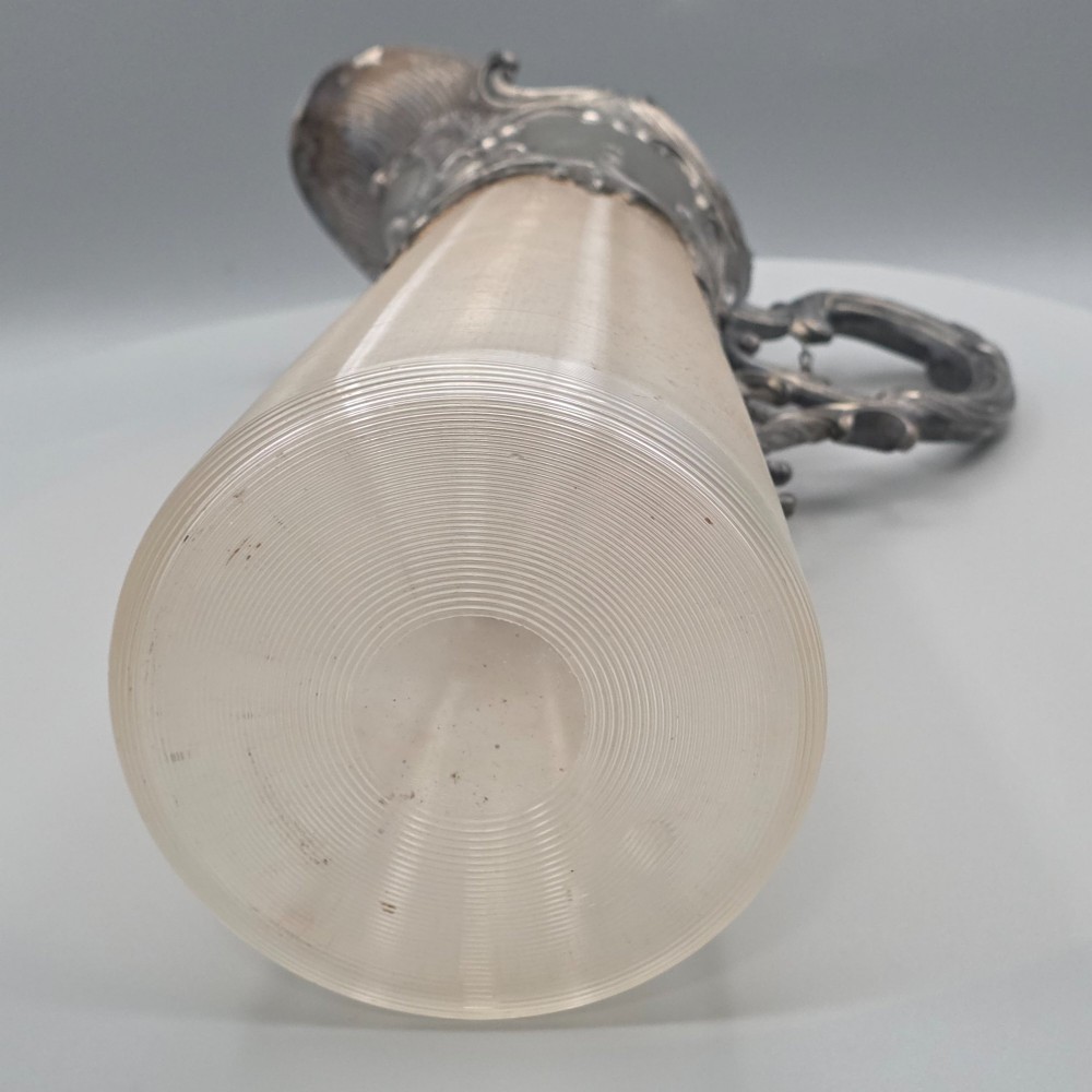 An antique French Rococo style silver-plated claret jug featuring a tapered ribbed clear glass body and an ornate scrolling silver spout and handle. View XIV