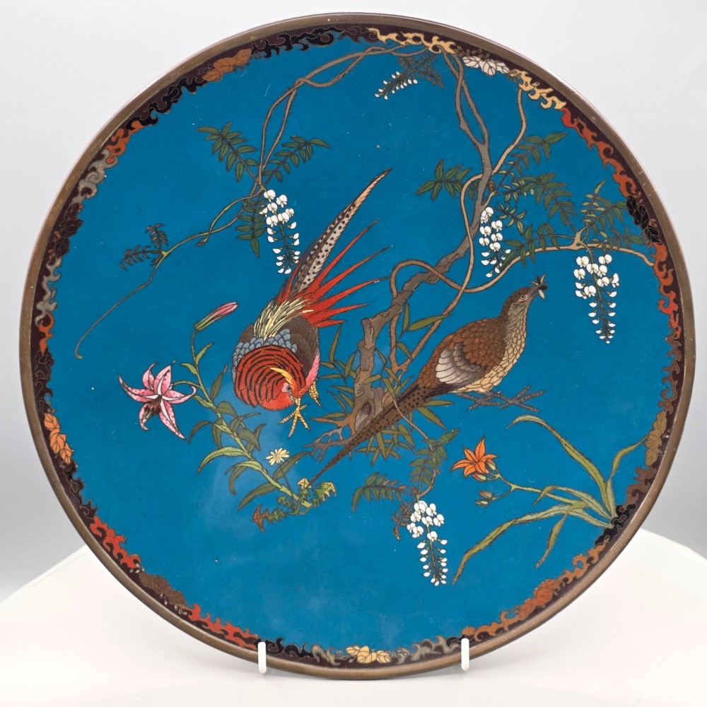 A circular Japanese Meiji period cloisonne enamel charger depicting birds perched on branches with flowers against a bright blue background.