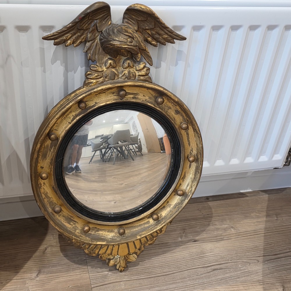 A circular convex mirror set in a gilded frame decorated with ball mouldings, an inner ebonised slip, topped with a carved eagle cresting. View II