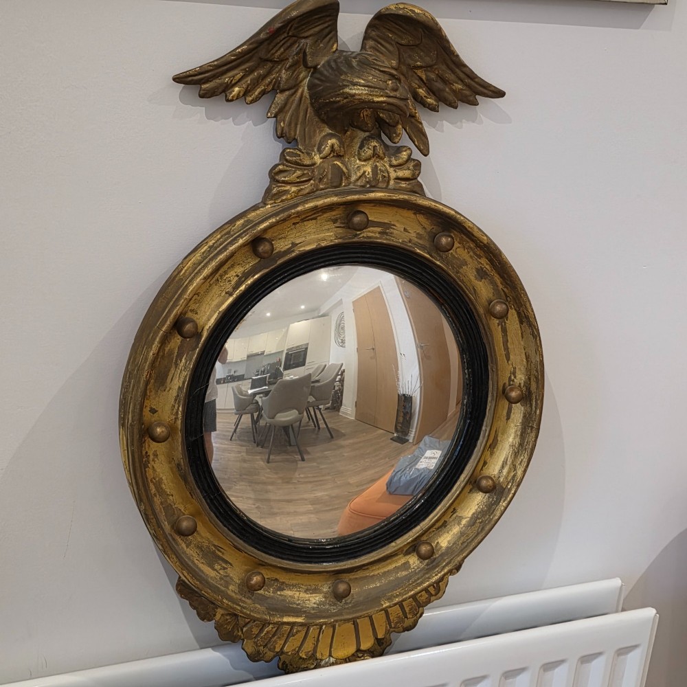 A circular convex mirror set in a gilded frame decorated with ball mouldings, an inner ebonised slip, topped with a carved eagle cresting. View III