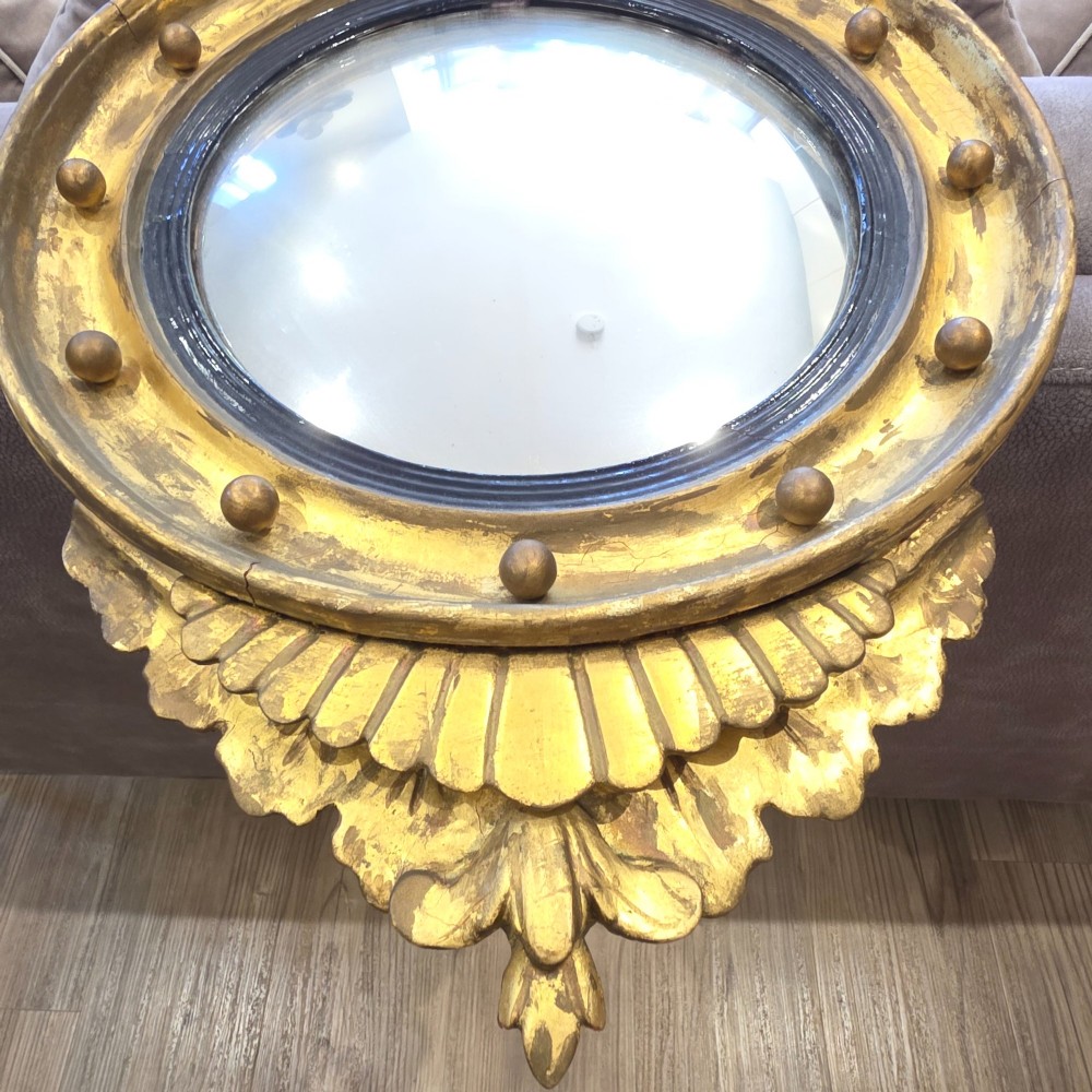 A circular convex mirror set in a gilded frame decorated with ball mouldings, an inner ebonised slip, topped with a carved eagle cresting. View IV