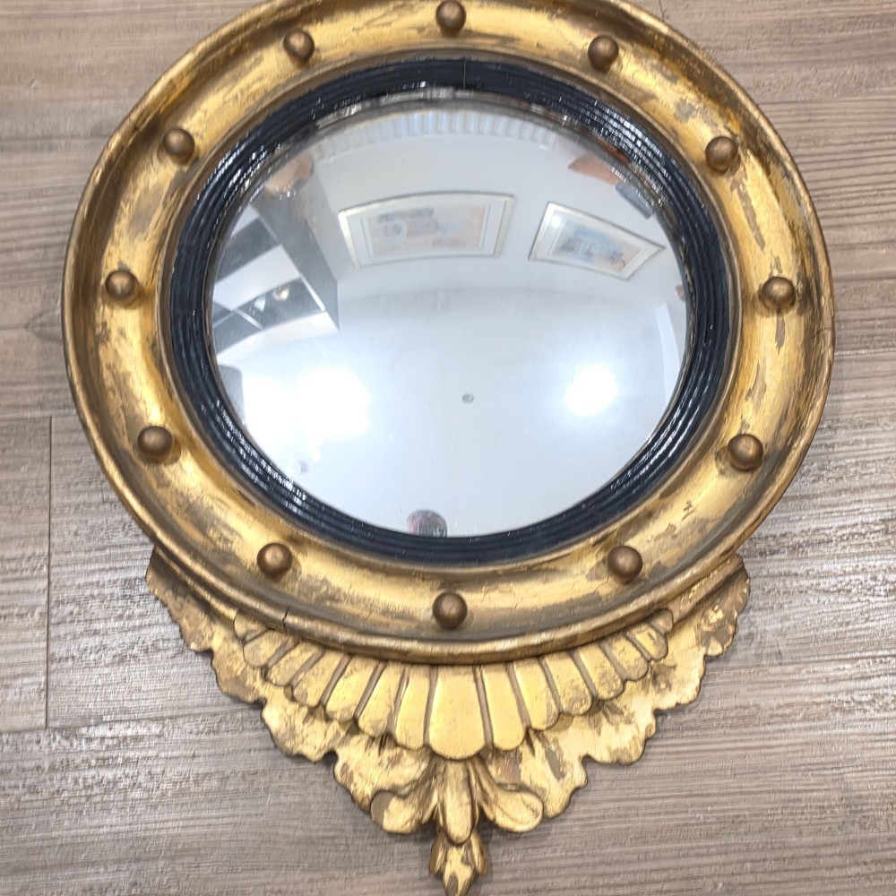 A circular convex mirror set in a gilded frame decorated with ball mouldings, an inner ebonised slip, topped with a carved eagle cresting. View V