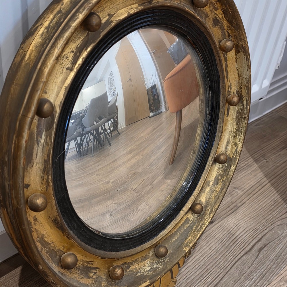 A circular convex mirror set in a gilded frame decorated with ball mouldings, an inner ebonised slip, topped with a carved eagle cresting. View VIII
