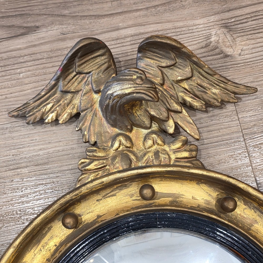 A circular convex mirror set in a gilded frame decorated with ball mouldings, an inner ebonised slip, topped with a carved eagle cresting. View VI