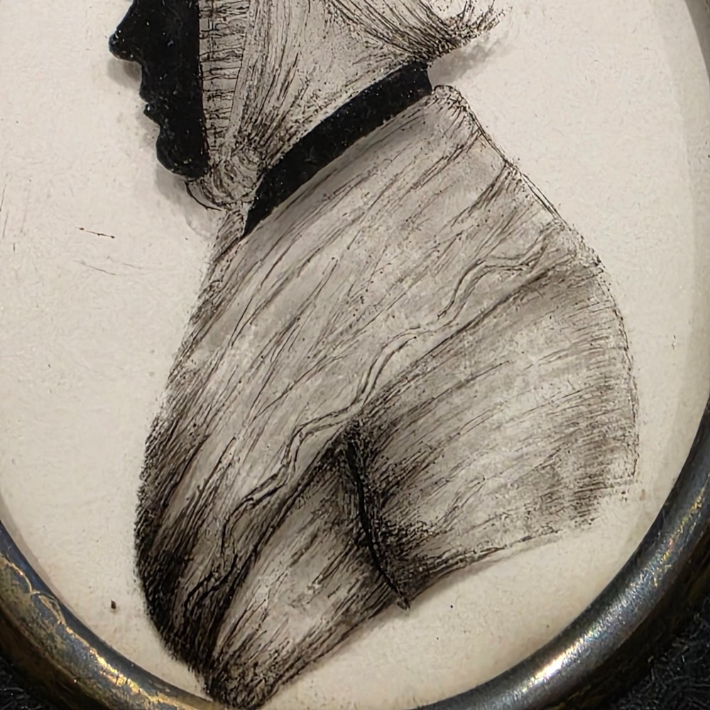 An antique oval Georgian silhouette portrait depicting a woman in profile wearing a bonnet, rendered via reverse painting on glass within a gilded bezel. View IV