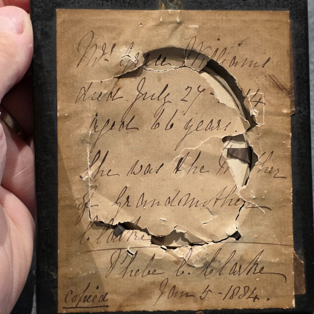 An antique oval Georgian silhouette portrait depicting a woman in profile wearing a bonnet, rendered via reverse painting on glass within a gilded bezel. View VI