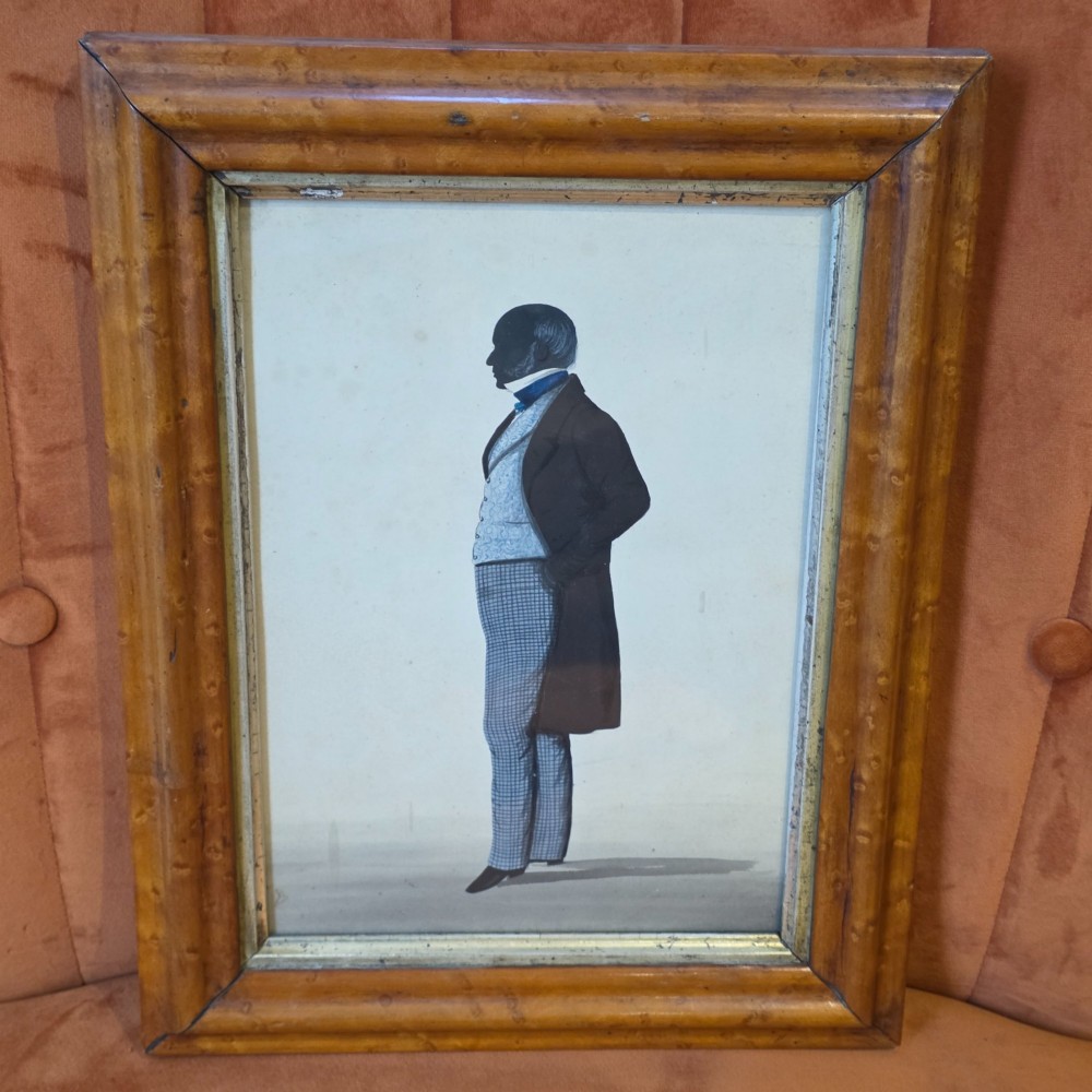 A framed full-length silhouette portrait of a gentleman in 19th-century costume presented in a birds eye maple frame.