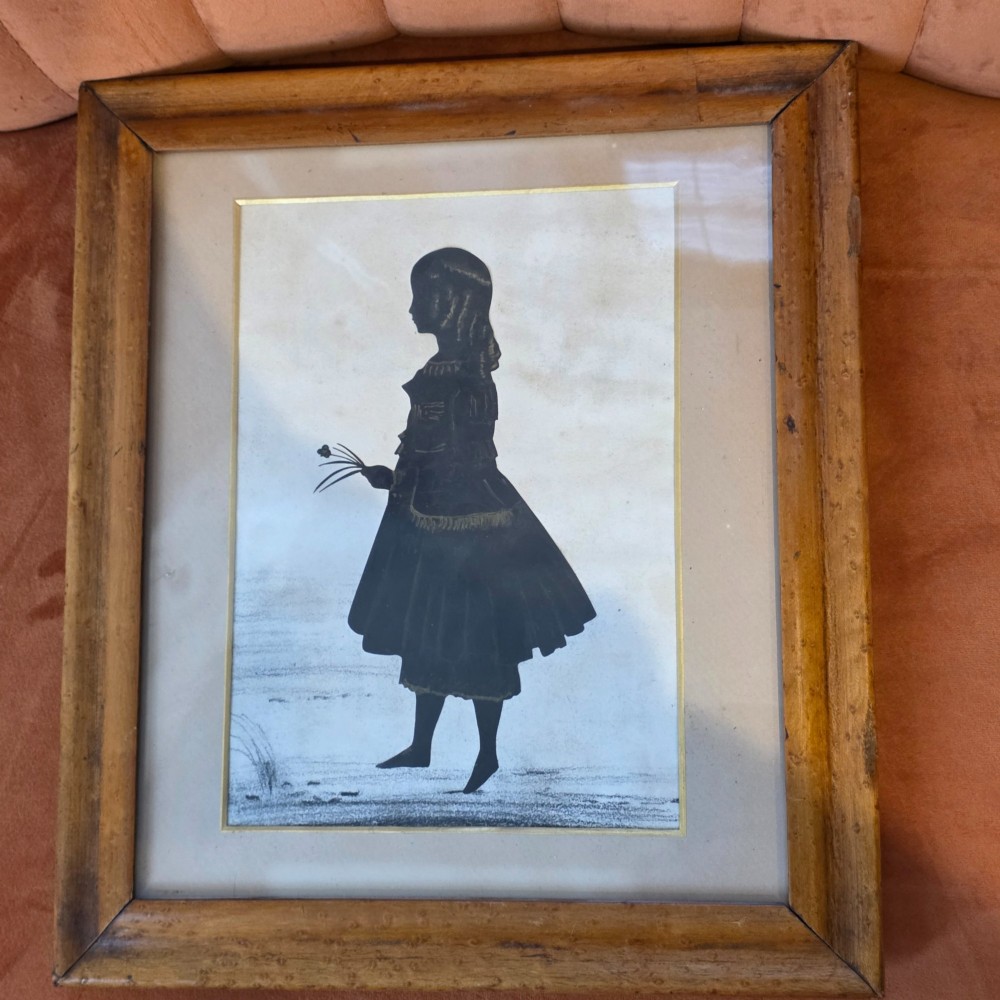 A 19th-century full-length cut-paper silhouette portrait of a young girl holding flowers, displayed in a glazed wooden frame with a gold inner slip. View III