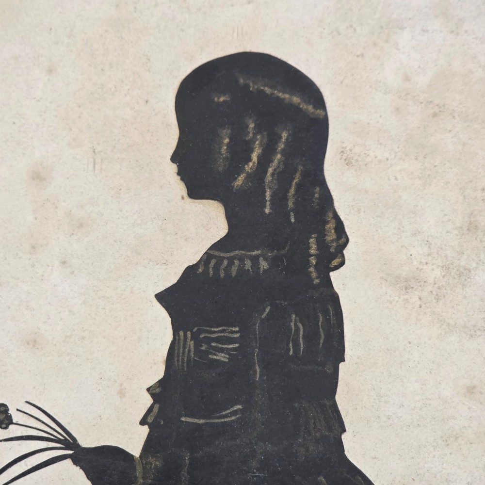 A 19th-century full-length cut-paper silhouette portrait of a young girl holding flowers, displayed in a glazed wooden frame with a gold inner slip. View V