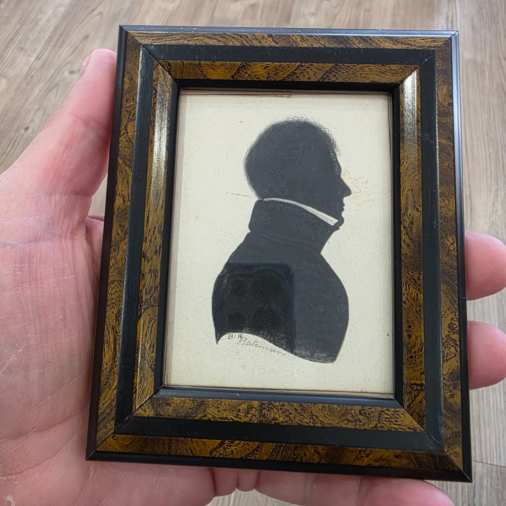 A small framed early 19th-century silhouette portrait depicting the right profile of a gentleman in a high-collared coat, presented in a decorated wood frame. View II