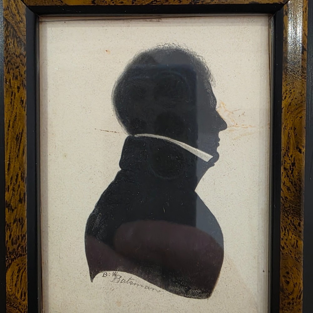 A small framed early 19th-century silhouette portrait depicting the right profile of a gentleman in a high-collared coat, presented in a decorated wood frame. View III