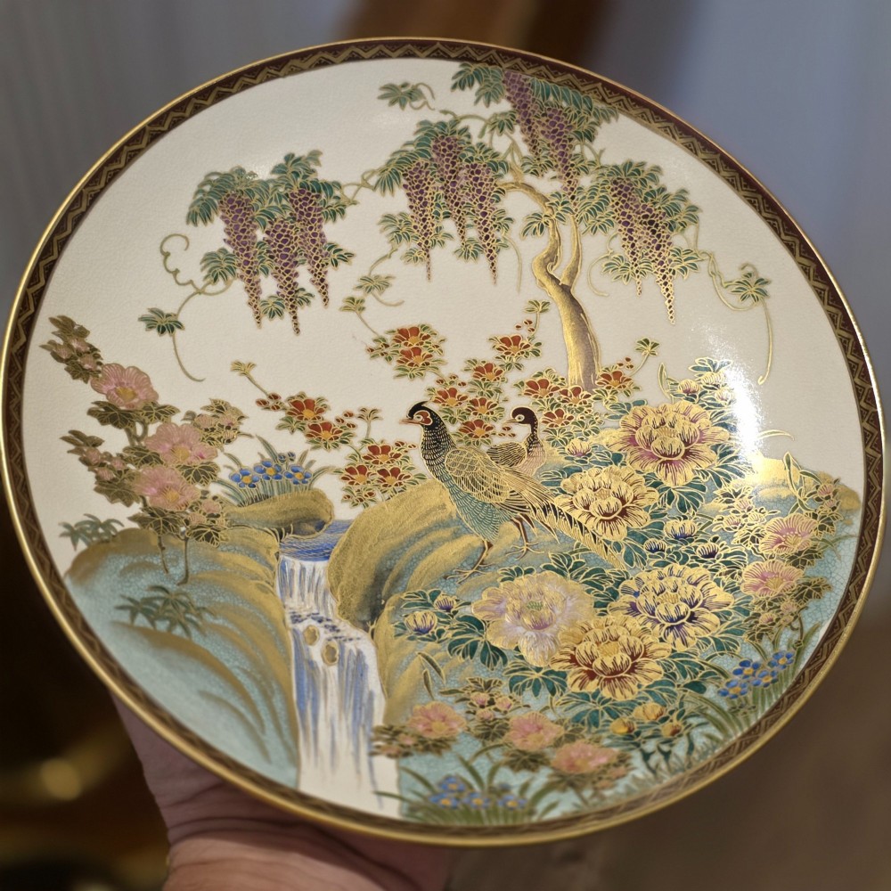 A circular Satsuma earthenware dish decorated with hand-painted pheasants, wisteria, flowers, and a waterfall with gilt accents.