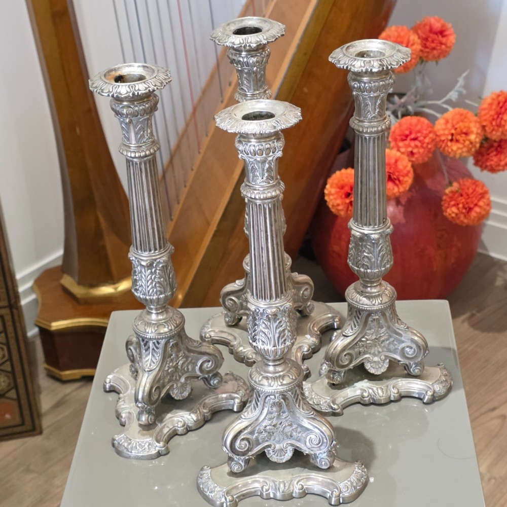A set of four silver candlesticks with fluted columns and ornate leaf details set on molded tripod bases. View II