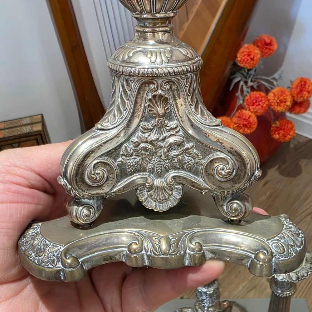 A set of four silver candlesticks with fluted columns and ornate leaf details set on molded tripod bases. View V