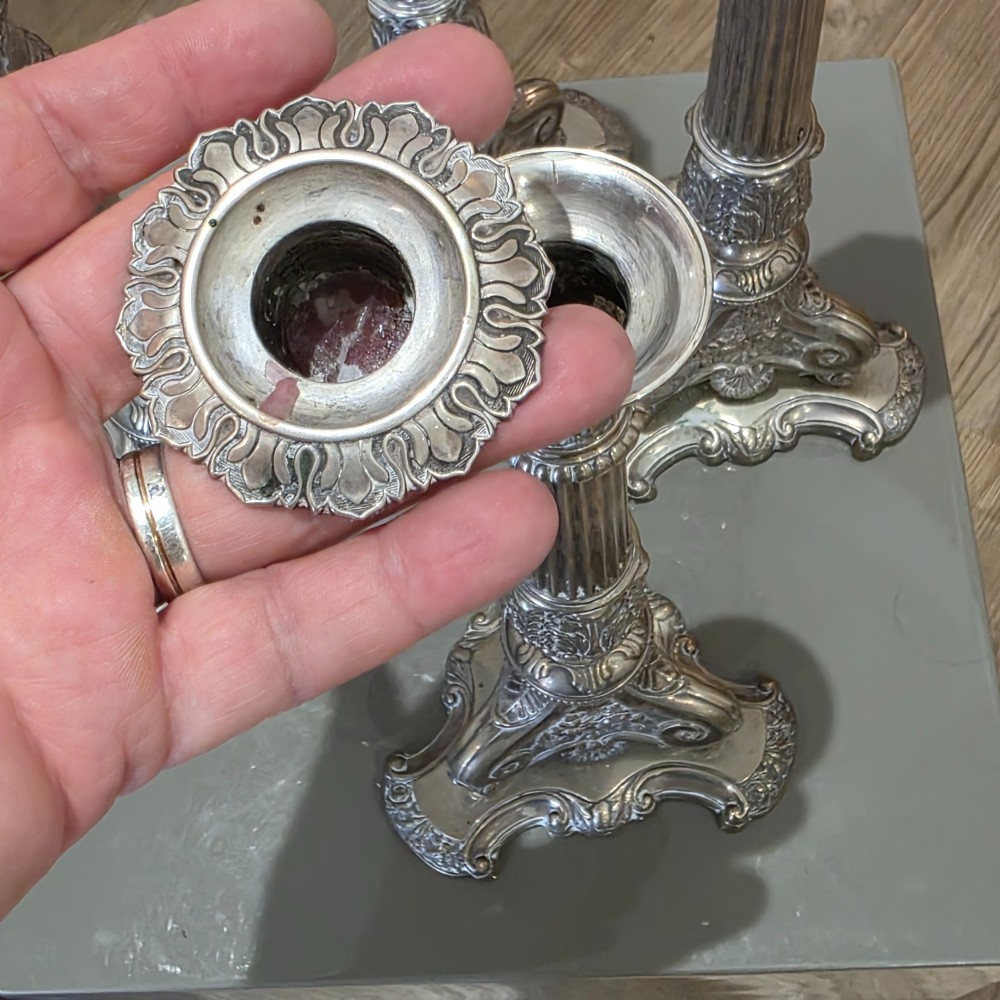 A set of four silver candlesticks with fluted columns and ornate leaf details set on molded tripod bases. View VII