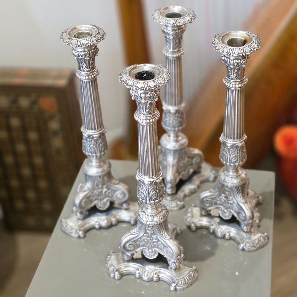 A set of four silver candlesticks with fluted columns and ornate leaf details set on molded tripod bases. View VIII