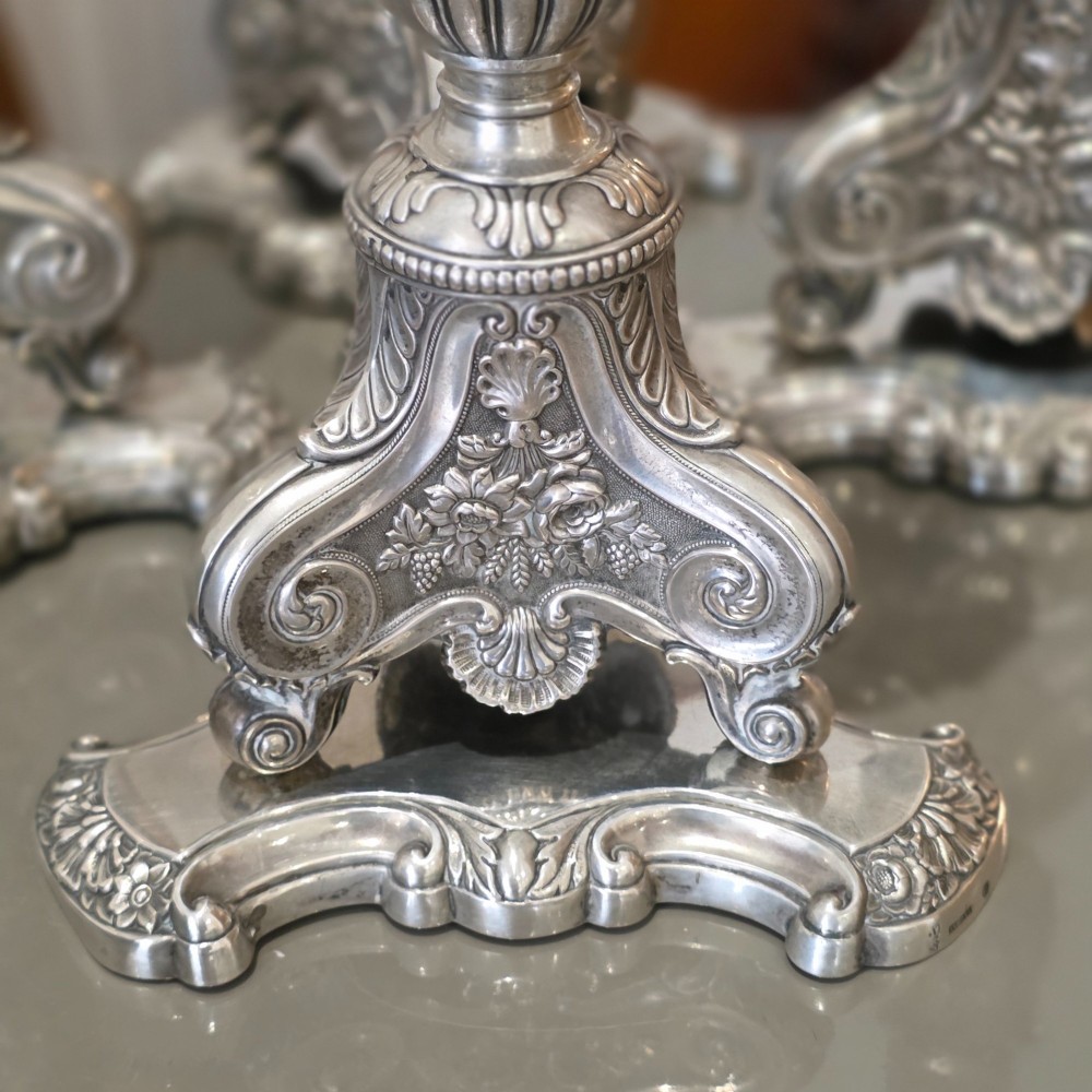 A set of four silver candlesticks with fluted columns and ornate leaf details set on molded tripod bases. View IX