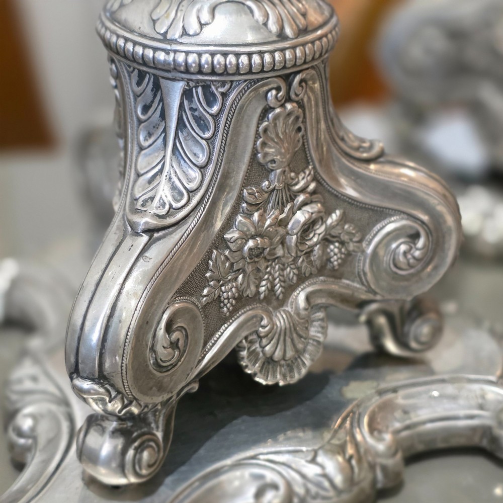 A set of four silver candlesticks with fluted columns and ornate leaf details set on molded tripod bases. View X