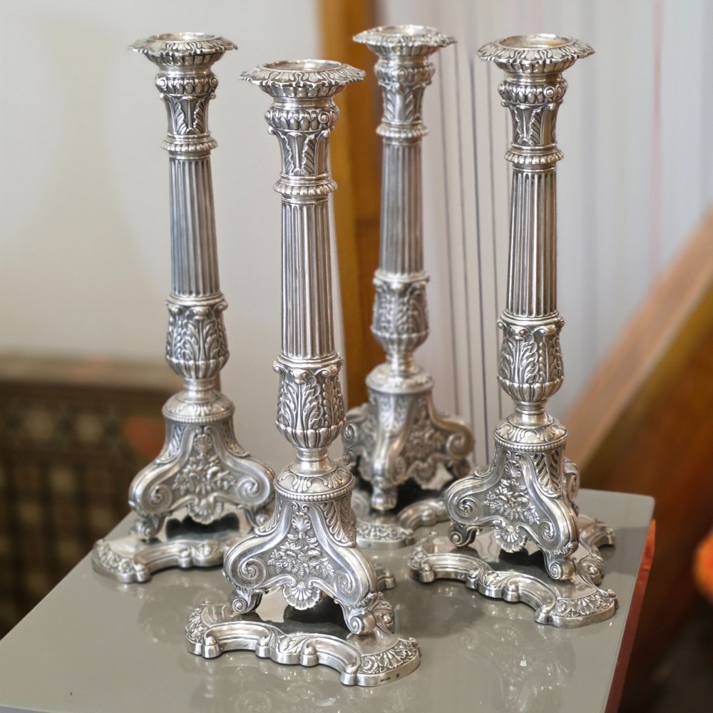 A set of four silver candlesticks with fluted columns and ornate leaf details set on molded tripod bases. View XI