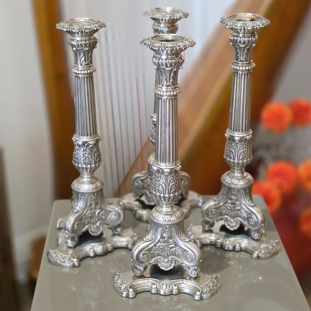 A set of four silver candlesticks with fluted columns and ornate leaf details set on molded tripod bases. View XII