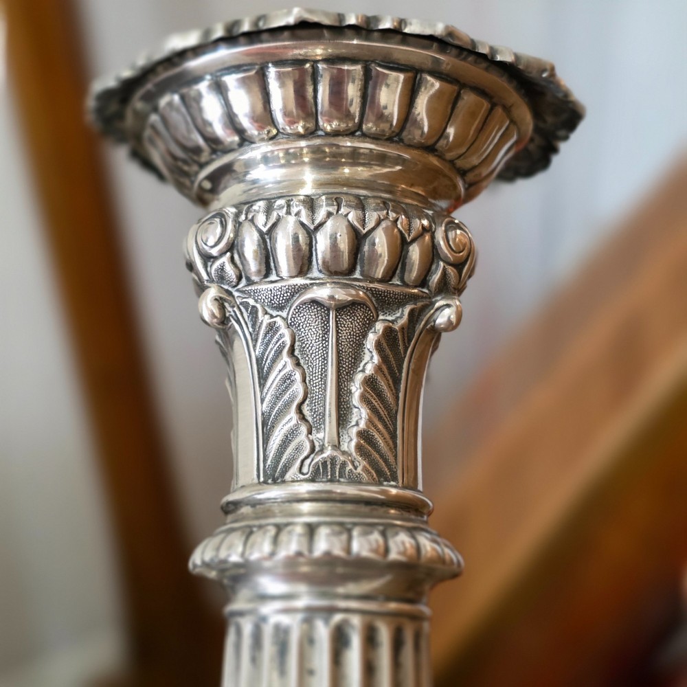 A set of four silver candlesticks with fluted columns and ornate leaf details set on molded tripod bases. View XIV