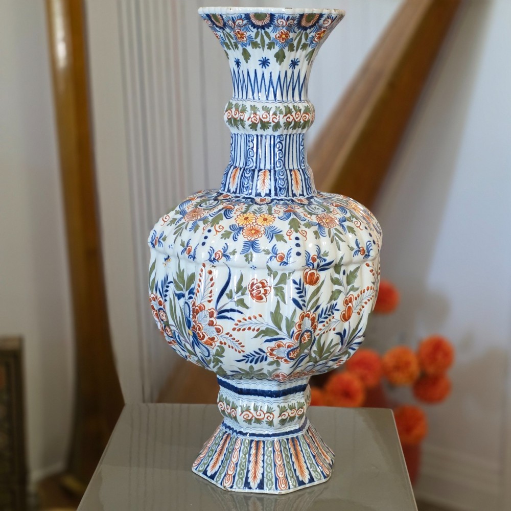 A tall nineteenth-century polychrome Delft earthenware vase featuring a fluted ribbed neck and bulbous body decorated with hand-painted floral motifs in blue, green, and orange on a white glazed ground.