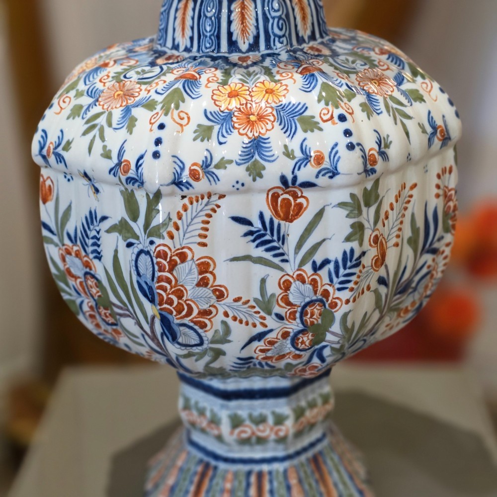 A tall nineteenth-century polychrome Delft earthenware vase featuring a fluted ribbed neck and bulbous body decorated with hand-painted floral motifs in blue, green, and orange on a white glazed ground. View IV