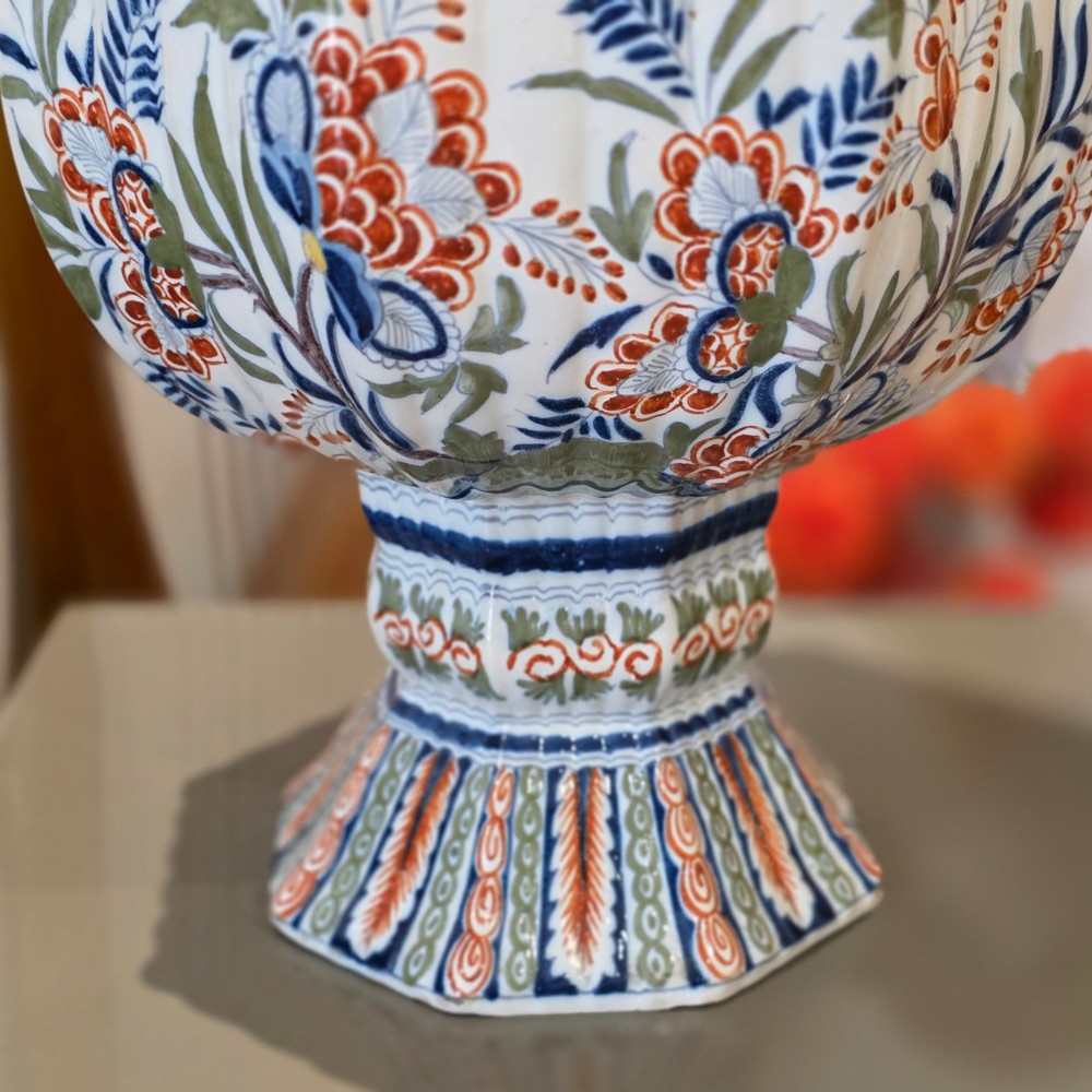 A tall nineteenth-century polychrome Delft earthenware vase featuring a fluted ribbed neck and bulbous body decorated with hand-painted floral motifs in blue, green, and orange on a white glazed ground. View V