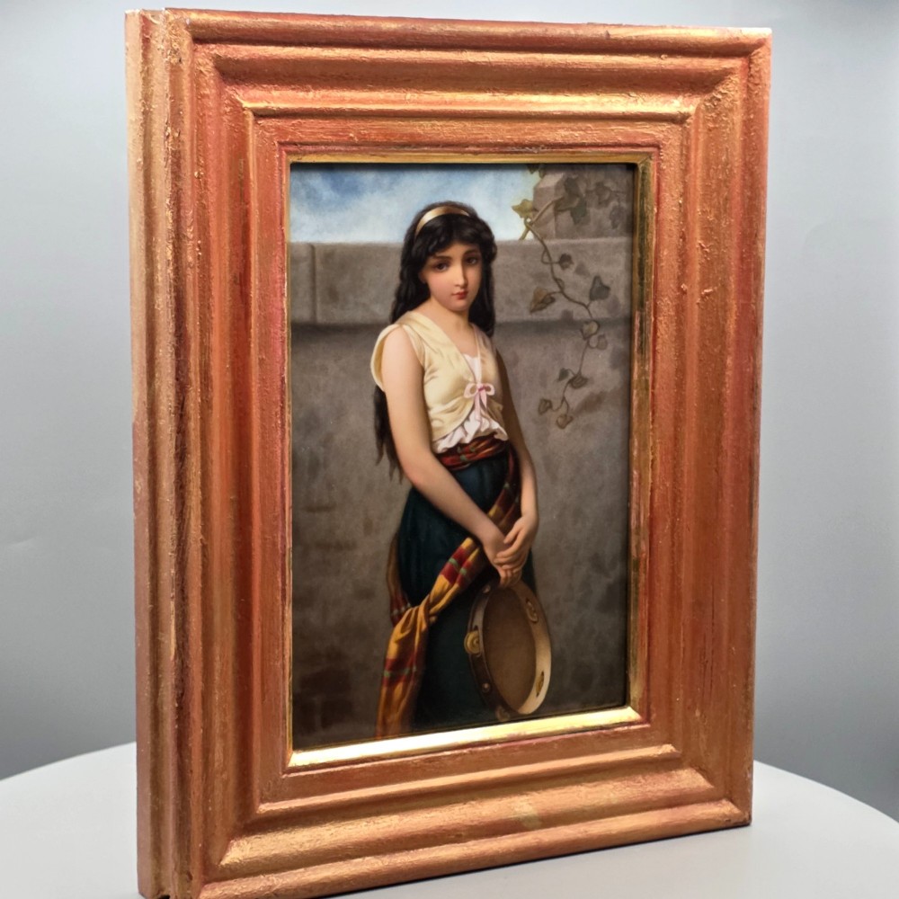 A rectangular hand-painted porcelain plaque depicting a young woman with a tambourine, set within a thick moulded gilt frame.