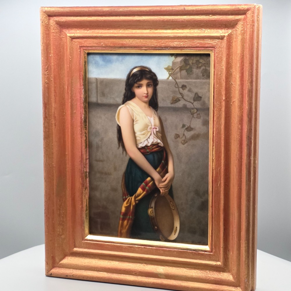 A rectangular hand-painted porcelain plaque depicting a young woman with a tambourine, set within a thick moulded gilt frame. View VI