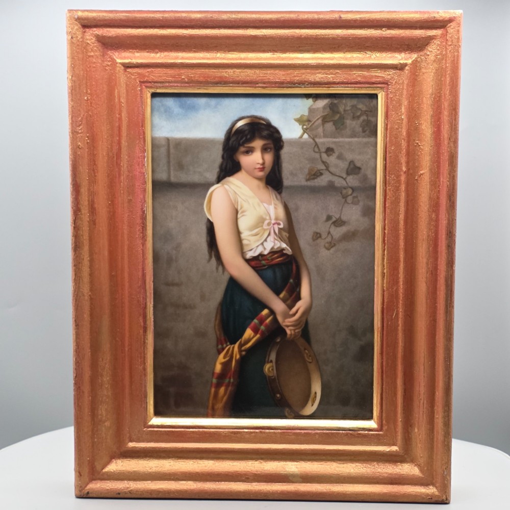 A rectangular hand-painted porcelain plaque depicting a young woman with a tambourine, set within a thick moulded gilt frame. View VII