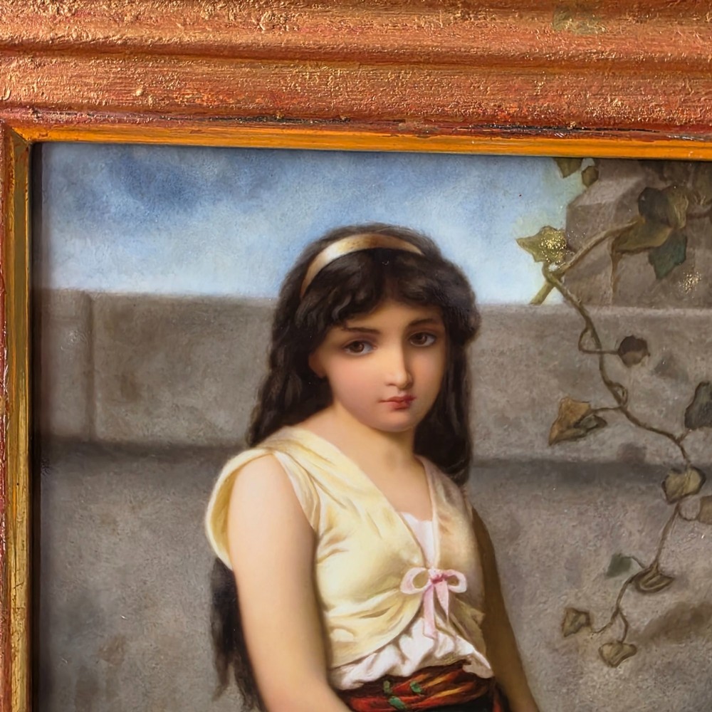 A rectangular hand-painted porcelain plaque depicting a young woman with a tambourine, set within a thick moulded gilt frame. View X