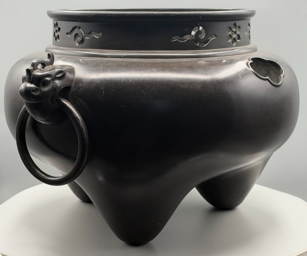 A dark patinated bronze tripod tea brazier featuring cast lion mask handles with loose ring pulls and pierced decorative motifs along the collar. View IV