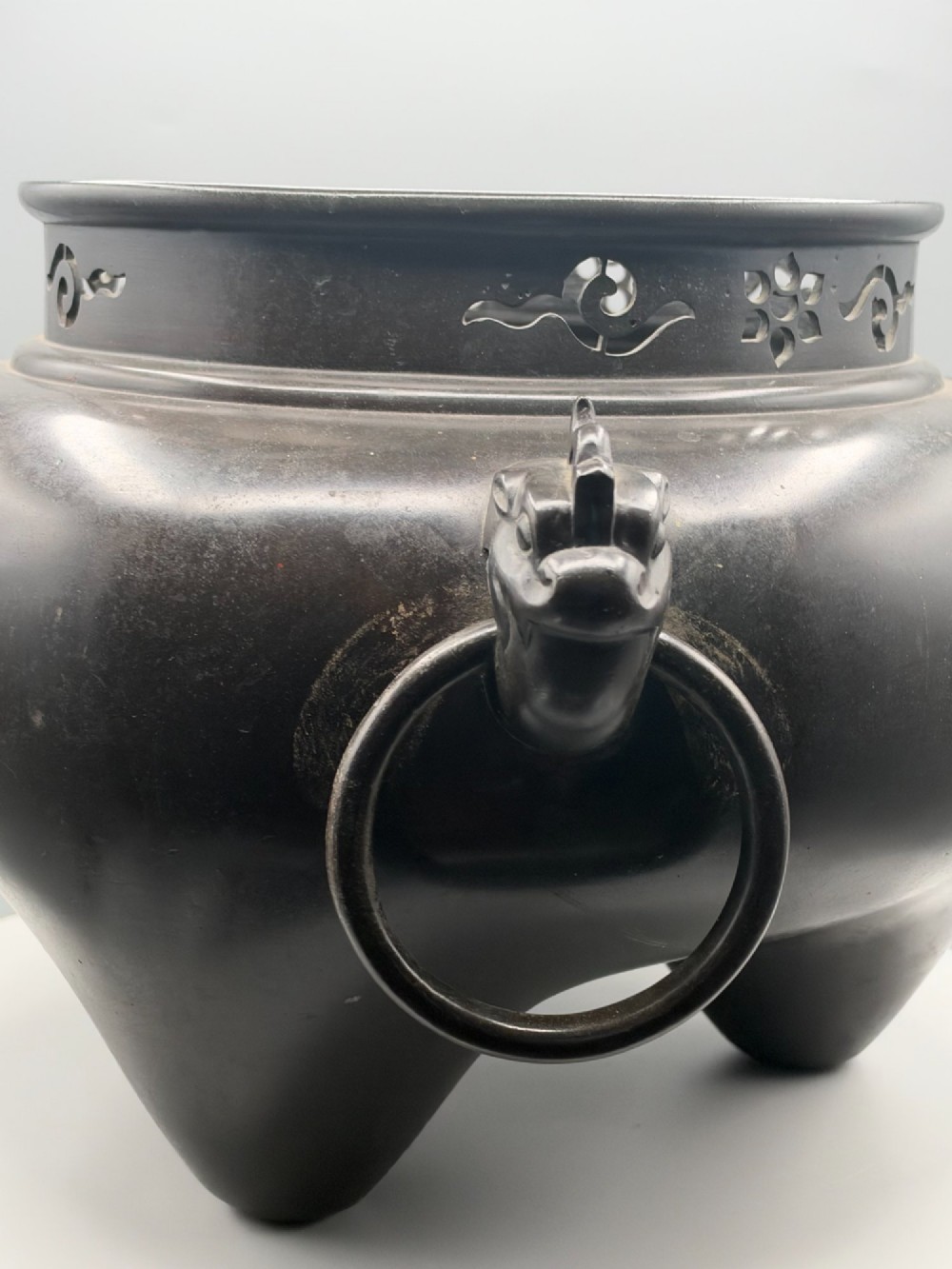A dark patinated bronze tripod tea brazier featuring cast lion mask handles with loose ring pulls and pierced decorative motifs along the collar. View VI
