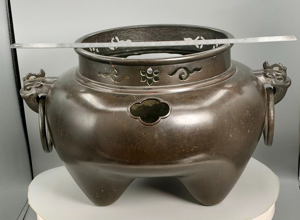 A dark patinated bronze tripod tea brazier featuring cast lion mask handles with loose ring pulls and pierced decorative motifs along the collar. View IX