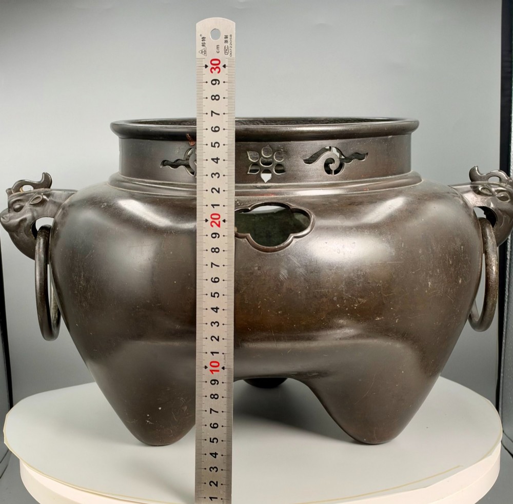 A dark patinated bronze tripod tea brazier featuring cast lion mask handles with loose ring pulls and pierced decorative motifs along the collar. View X