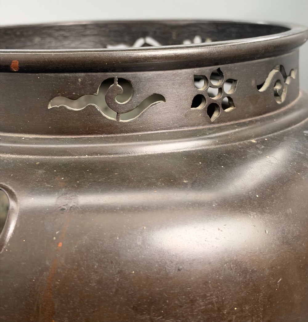 A dark patinated bronze tripod tea brazier featuring cast lion mask handles with loose ring pulls and pierced decorative motifs along the collar. View XI
