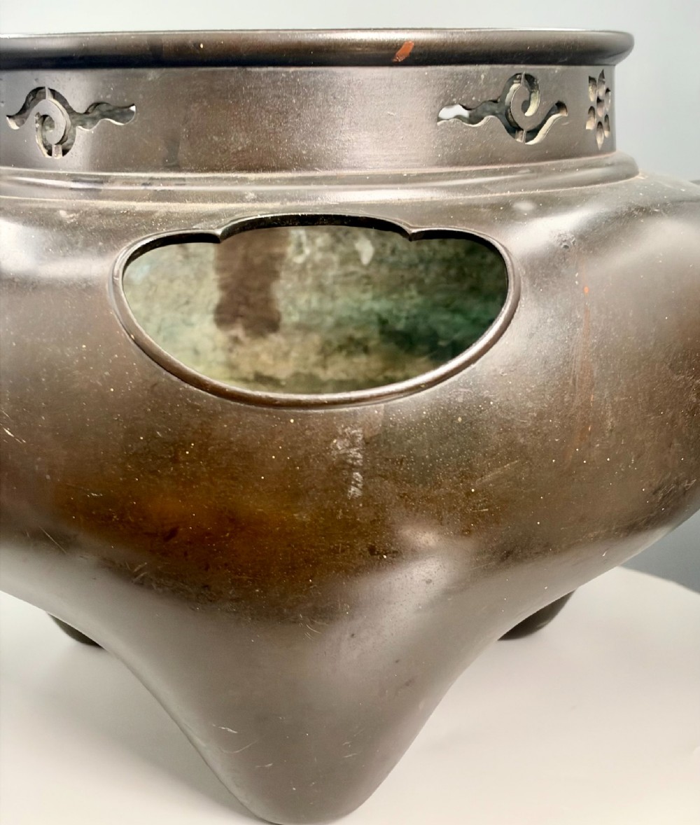A dark patinated bronze tripod tea brazier featuring cast lion mask handles with loose ring pulls and pierced decorative motifs along the collar. View XII