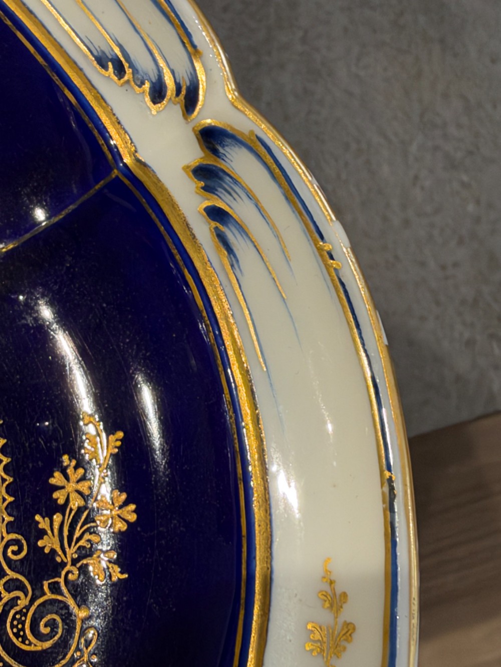 An oval French Sevres porcelain dish featuring a deep cobalt blue rim decorated with intricate gold leaf gilding surrounding a central hand-painted maritime harbour scene. View X