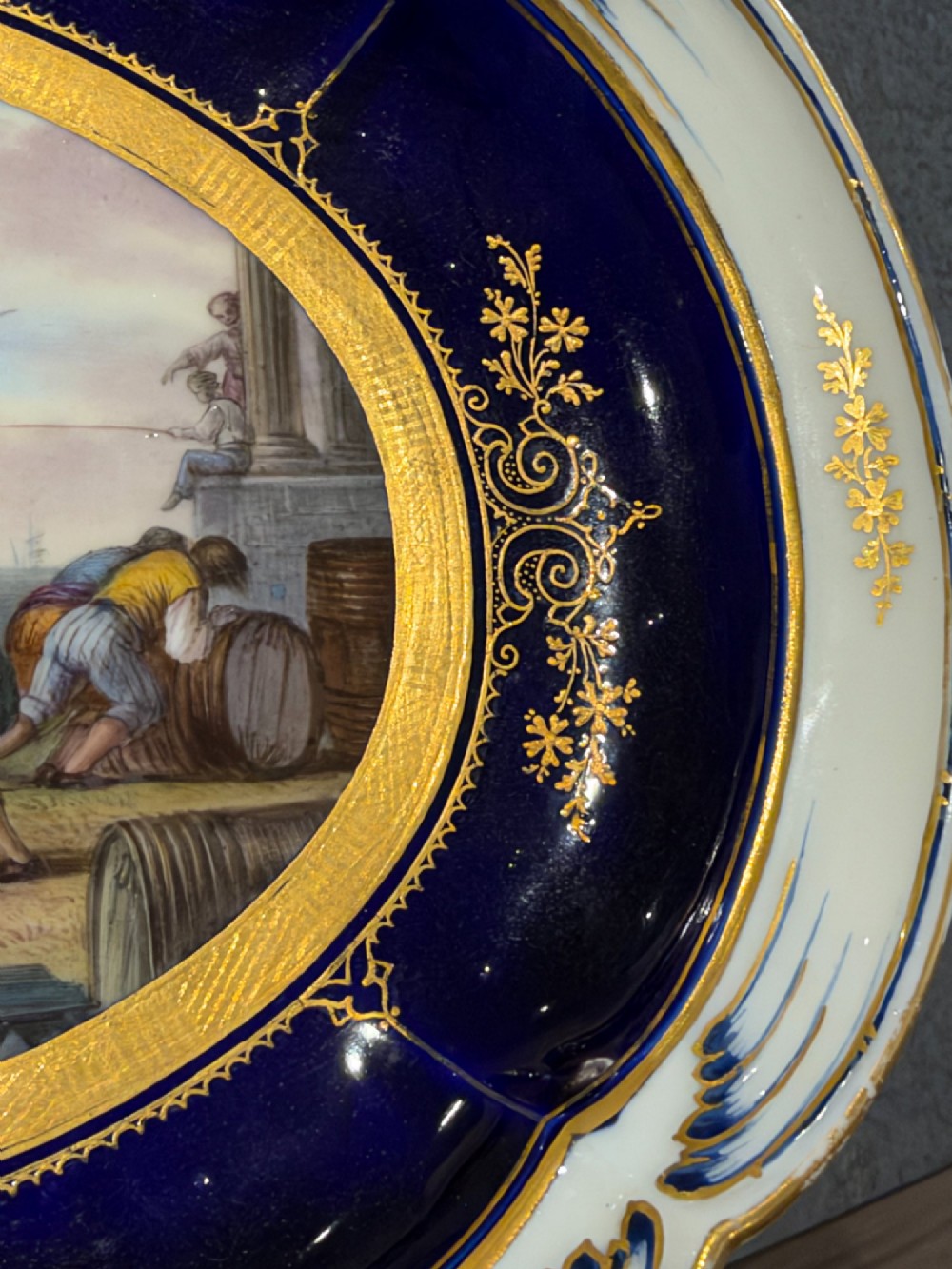 An oval French Sevres porcelain dish featuring a deep cobalt blue rim decorated with intricate gold leaf gilding surrounding a central hand-painted maritime harbour scene. View XI