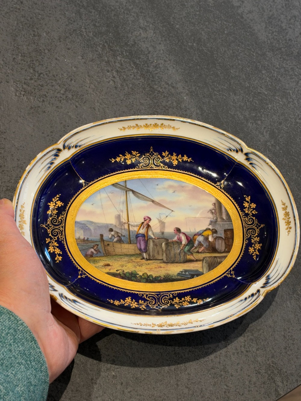 An oval French Sevres porcelain dish featuring a deep cobalt blue rim decorated with intricate gold leaf gilding surrounding a central hand-painted maritime harbour scene. View XIV