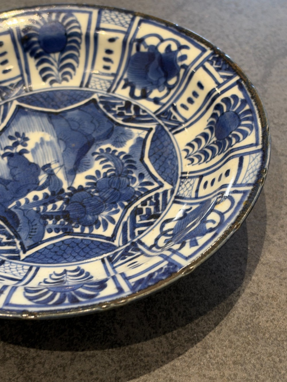 A circular 17th-century Chinese Kraak porcelain dish featuring underglaze cobalt blue panelled decoration surrounding a central landscape reserve. View IX