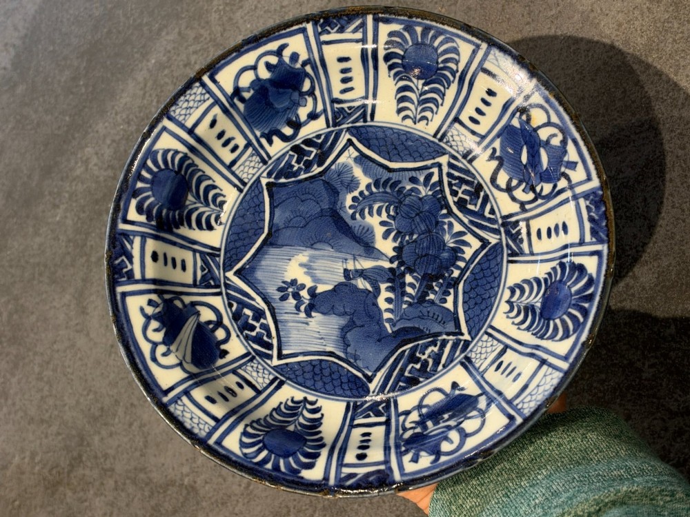 A circular 17th-century Chinese Kraak porcelain dish featuring underglaze cobalt blue panelled decoration surrounding a central landscape reserve. View II