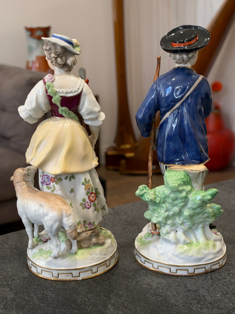 A pair of antique hand-painted German porcelain figures depicting a shepherdess with a lamb and a shepherd holding a basket, set on circular gilded bases. View IV