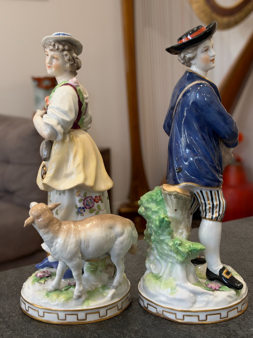 A pair of antique hand-painted German porcelain figures depicting a shepherdess with a lamb and a shepherd holding a basket, set on circular gilded bases. View VI