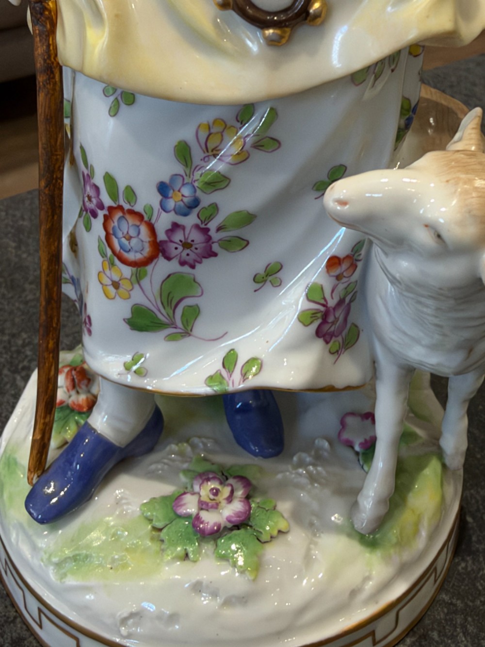 A pair of antique hand-painted German porcelain figures depicting a shepherdess with a lamb and a shepherd holding a basket, set on circular gilded bases. View X